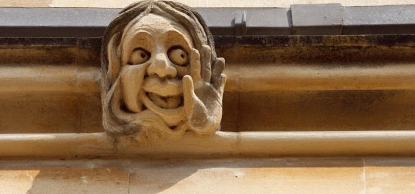A sandstone gargoyle with smiling face and upturned palm