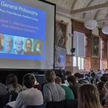 View of an audience in a hall with a slide projected on a large screen stating 'General Philosophy'
