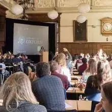 An audience member raises their hand in a busy lecture hall