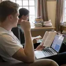 Two students sit with books and laptops