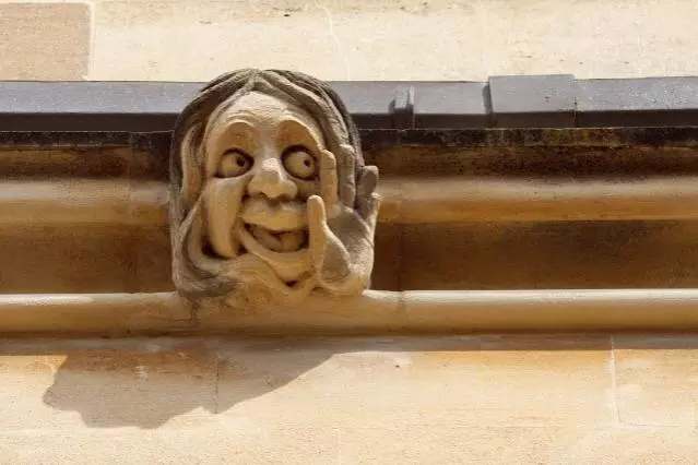 A sandstone gargoyle with smiling face and upturned palm