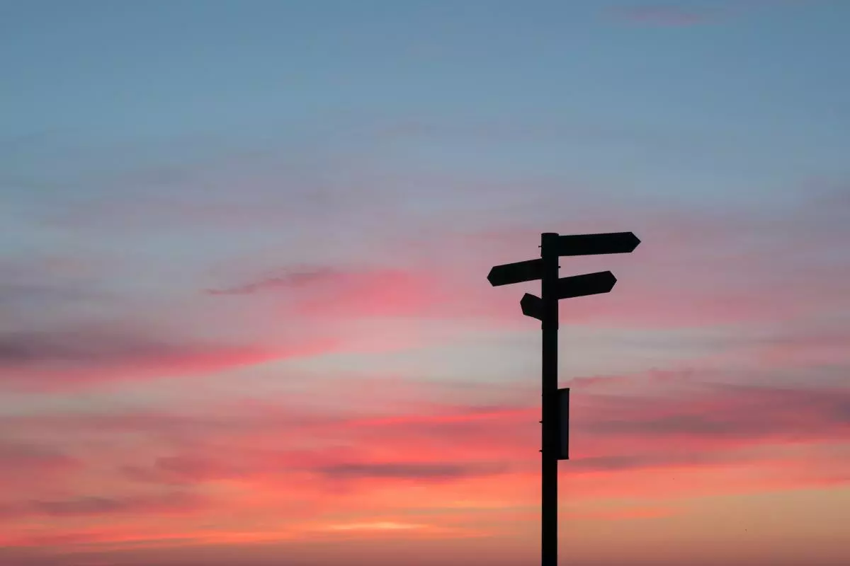 A signpost with four signs silhouetted against a sunset sky or oranges and blues